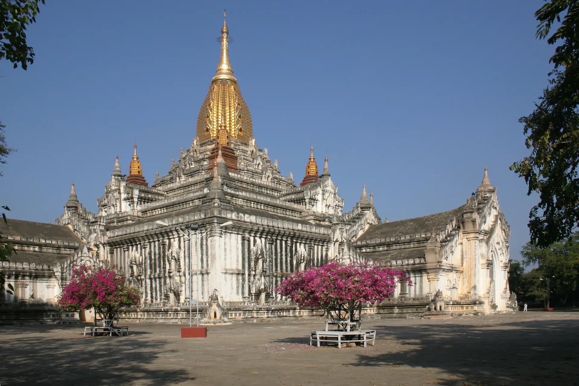 Templo Ananda elevándose contra el cielo azul con sus distintivas agujas doradas, paredes encaladas y planta cruciforme visible desde una perspectiva elevada