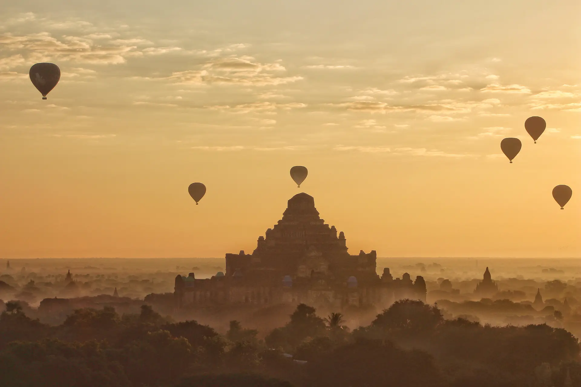 Múltiples globos aerostáticos flotando sobre las llanuras de templos de Bagan al amanecer, con pagodas y templos antiguos visibles abajo a través de la niebla matutina