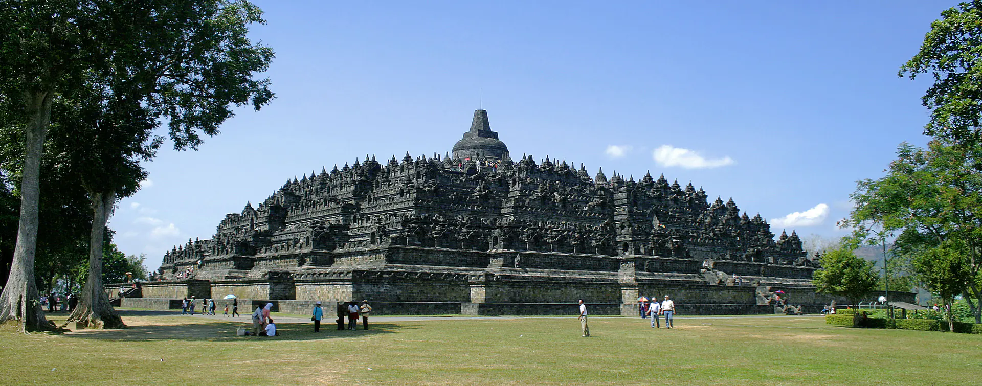 Vista aérea del Templo de Borobudur mostrando su masiva estructura de mandala con nueve plataformas apiladas, 72 estupas y el volcán Monte Merapi al fondo