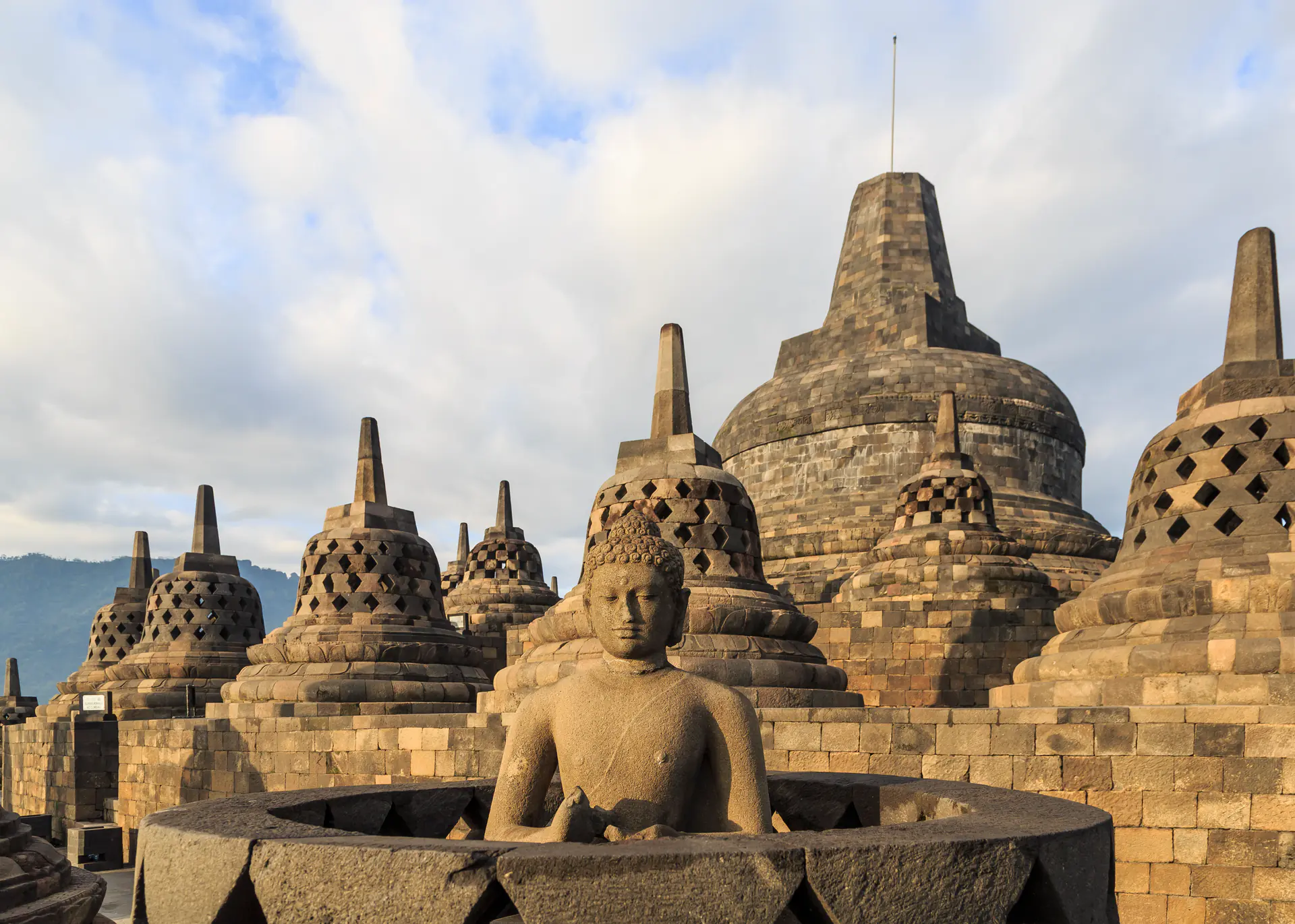 Vista de cerca de las distintivas estupas perforadas con forma de campana de Borobudur que contienen estatuas de Buda visibles a través de aberturas en forma de diamante contra el cielo azul