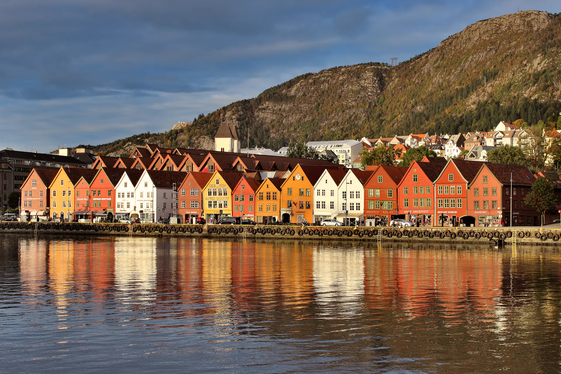 Coloridos edificios de madera de Bryggen reflejados en las aguas tranquilas del puerto de Bergen al atardecer, mostrando el icónico muelle comercial hanseático medieval