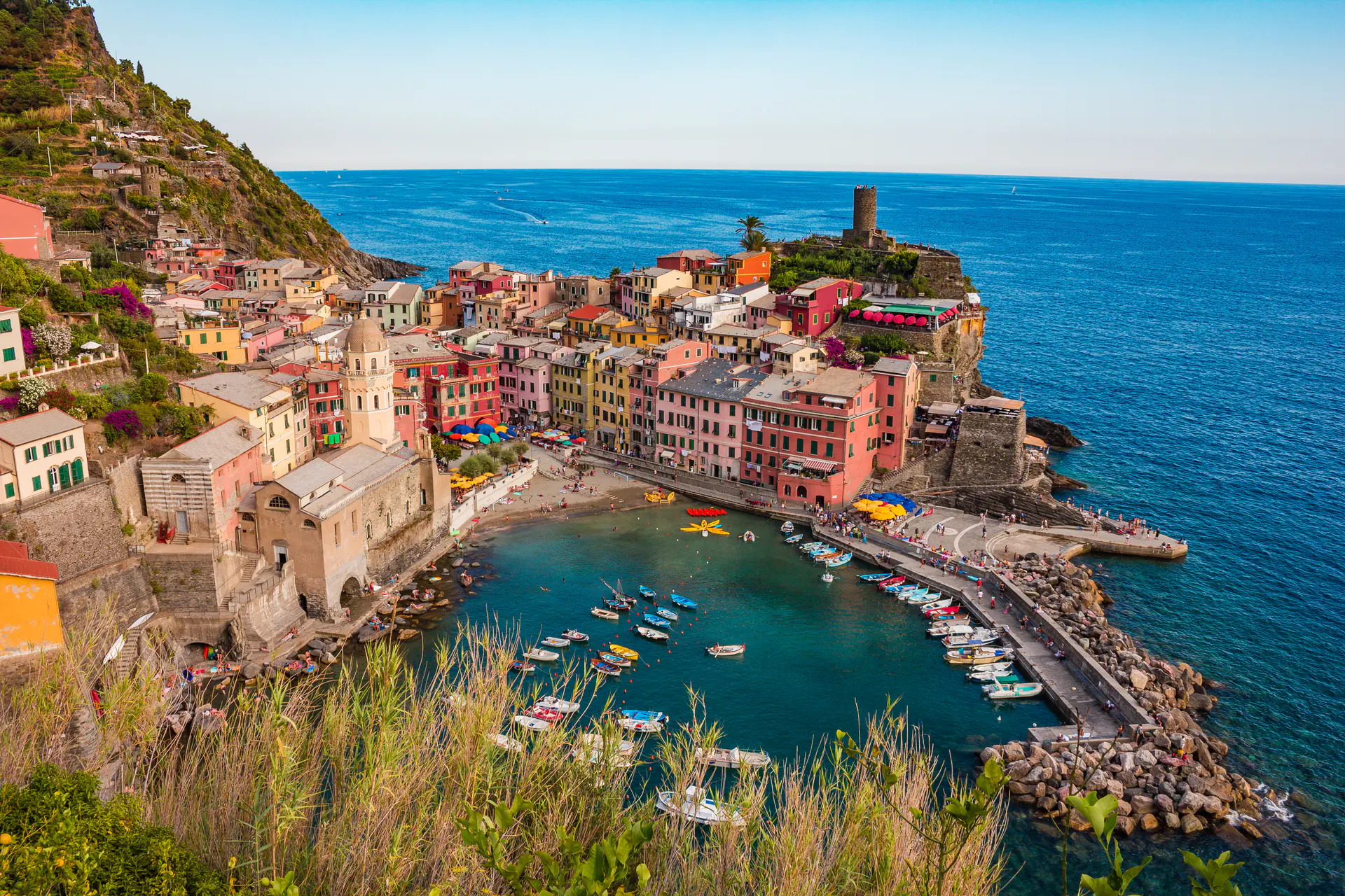 Traditional colorful tower houses of Vernazza cascading down to the picturesque harbor with boats and the Ligurian Sea