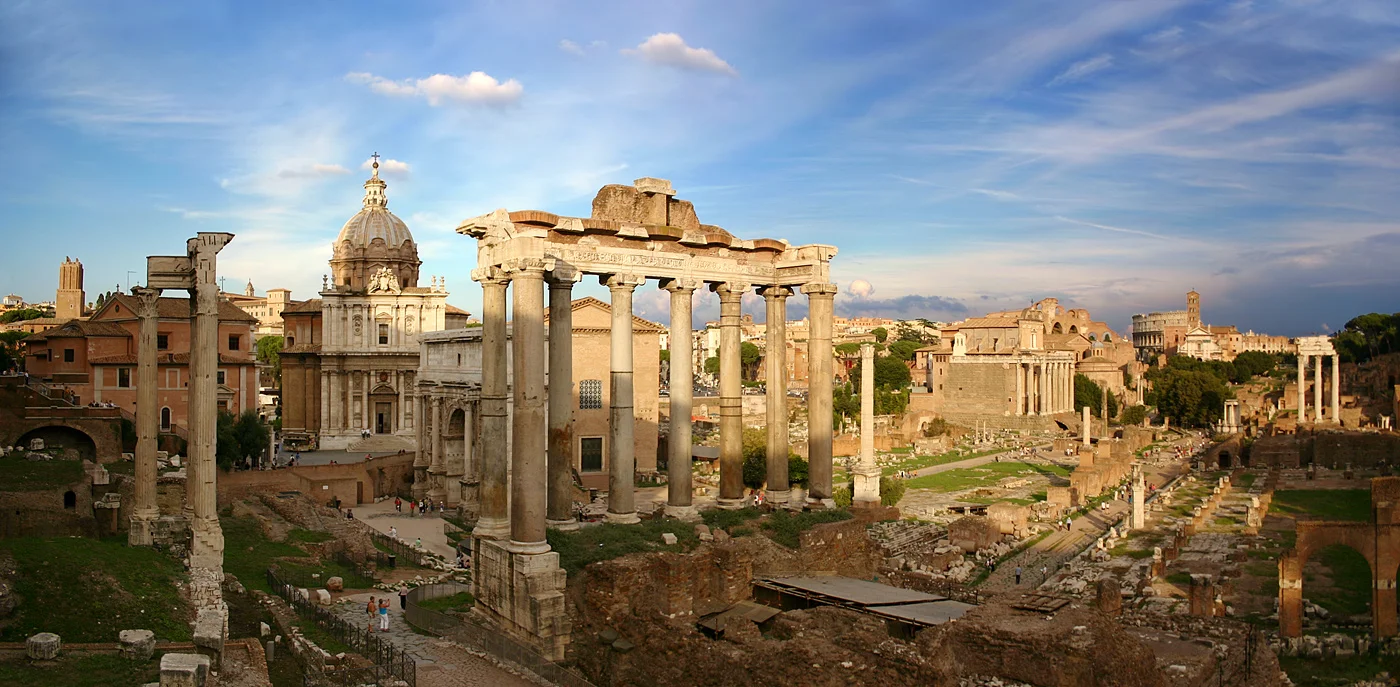 Vista panorámica del sitio arqueológico del Foro Romano mostrando ruinas de templos antiguos, columnas y la Via Sacra con el Coliseo visible al fondo