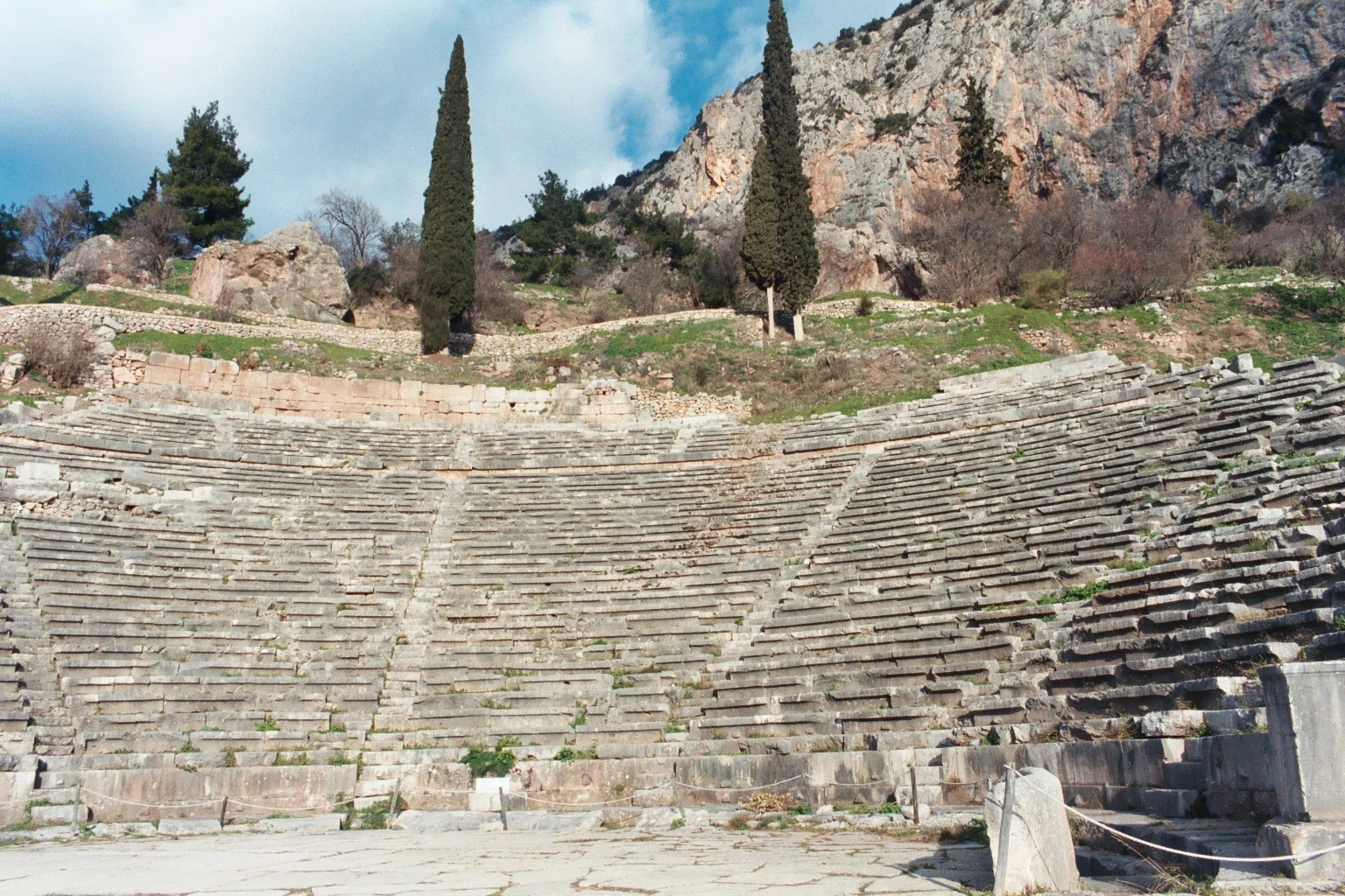 The ancient Greek theater at Delphi showing curved stone seating rows carved into the hillside with mountain views beyond