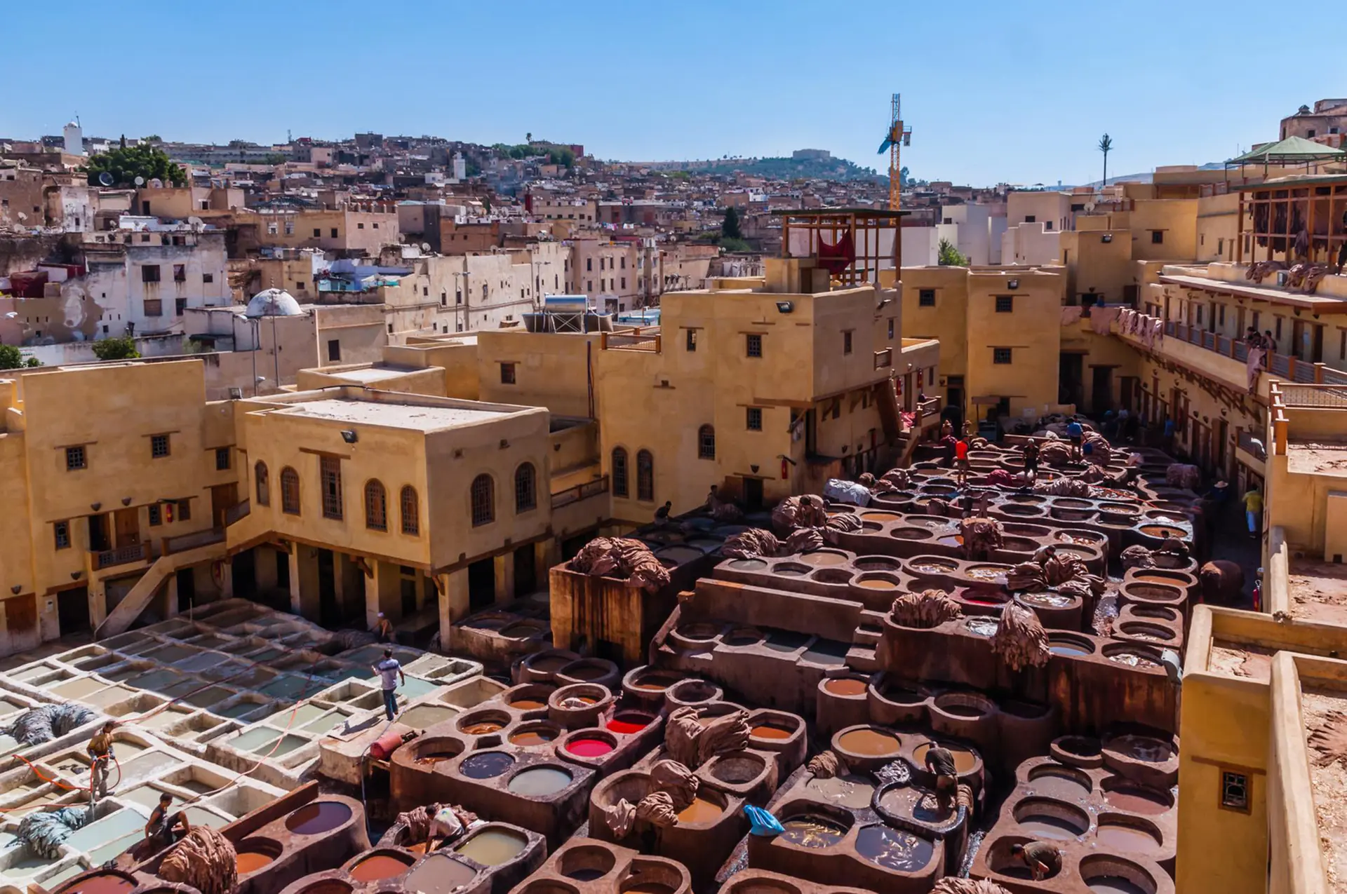 Aerial view of Chouara Tannery showing hundreds of circular stone vessels filled with vibrant colored dyes creating an iconic honeycomb pattern with workers processing leather