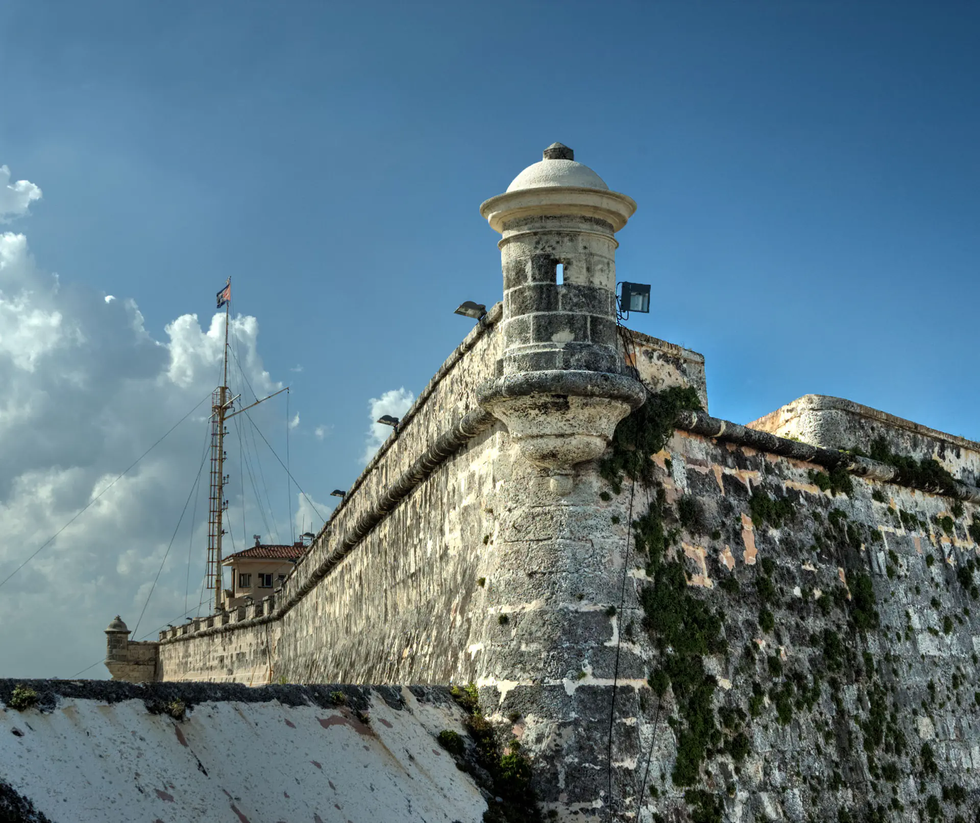 La fortaleza del Castillo del Morro con su icónico faro encaramado sobre acantilados rocosos con vista a la entrada del puerto de La Habana, con olas rompiendo contra las fortificaciones de piedra