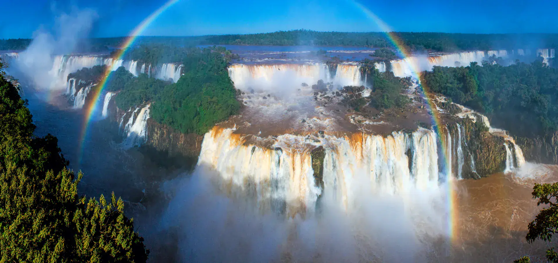 Vista aérea espectacular de las Cataratas del Iguazú con arcoíris formado por el rocío de las cascadas, mostrando el sistema completo de saltos desde arriba con la exuberante Selva Atlántica rodeando las cataratas