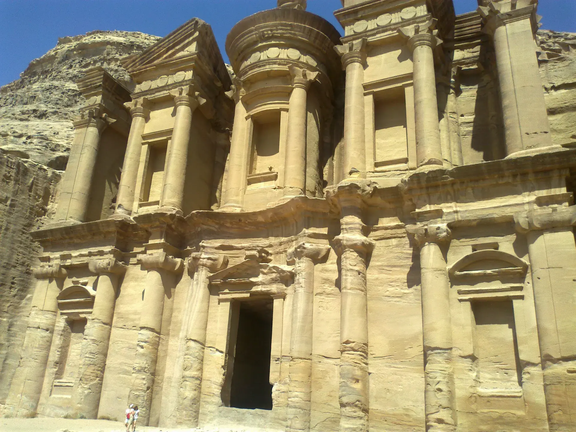 The massive Monastery (Ad-Deir) carved into Petra's sandstone cliffs, showing the largest rock-cut facade with visitors for scale