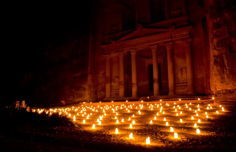 The Treasury of Petra illuminated by hundreds of candles at night, creating a magical atmospheric scene with the carved facade glowing against the dark rock