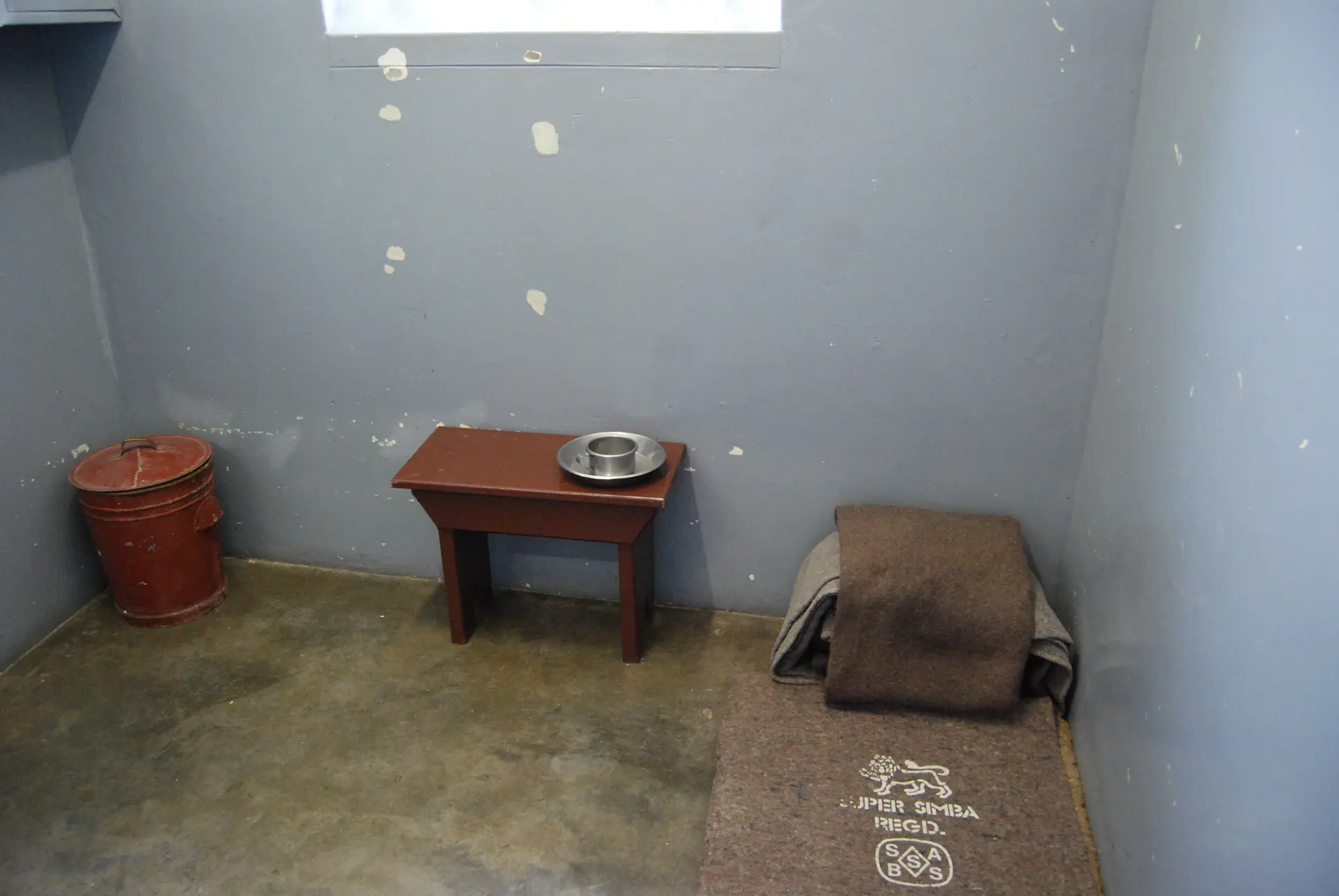 La pequeña celda de prisión número 5 donde Nelson Mandela estuvo encarcelado durante 18 años, mostrando las condiciones austeras con paredes de concreto y ventana con barrotes