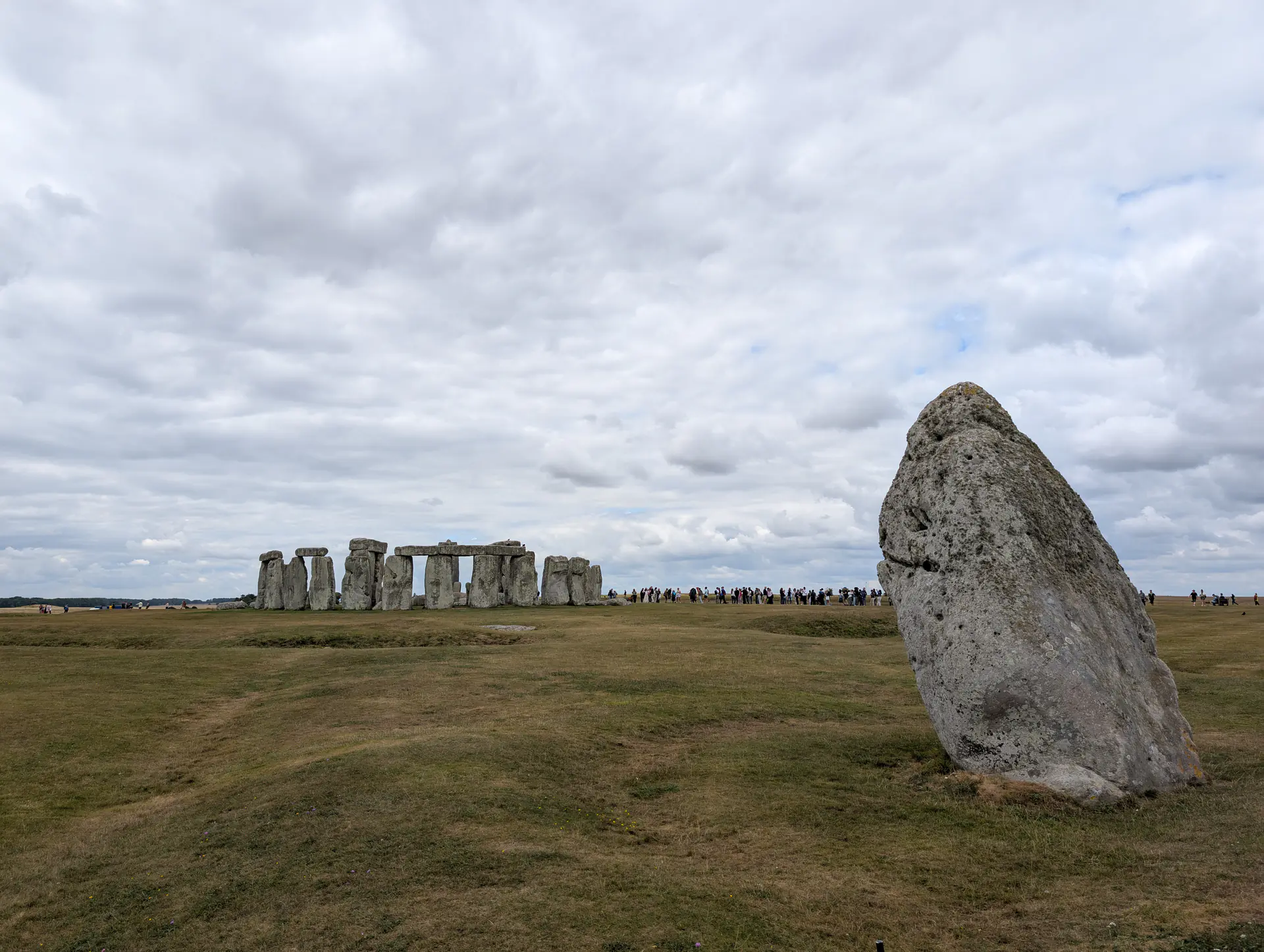 La Piedra del Talón erguida prominentemente en primer plano con el círculo de piedras de Stonehenge visible al fondo a través del campo de césped