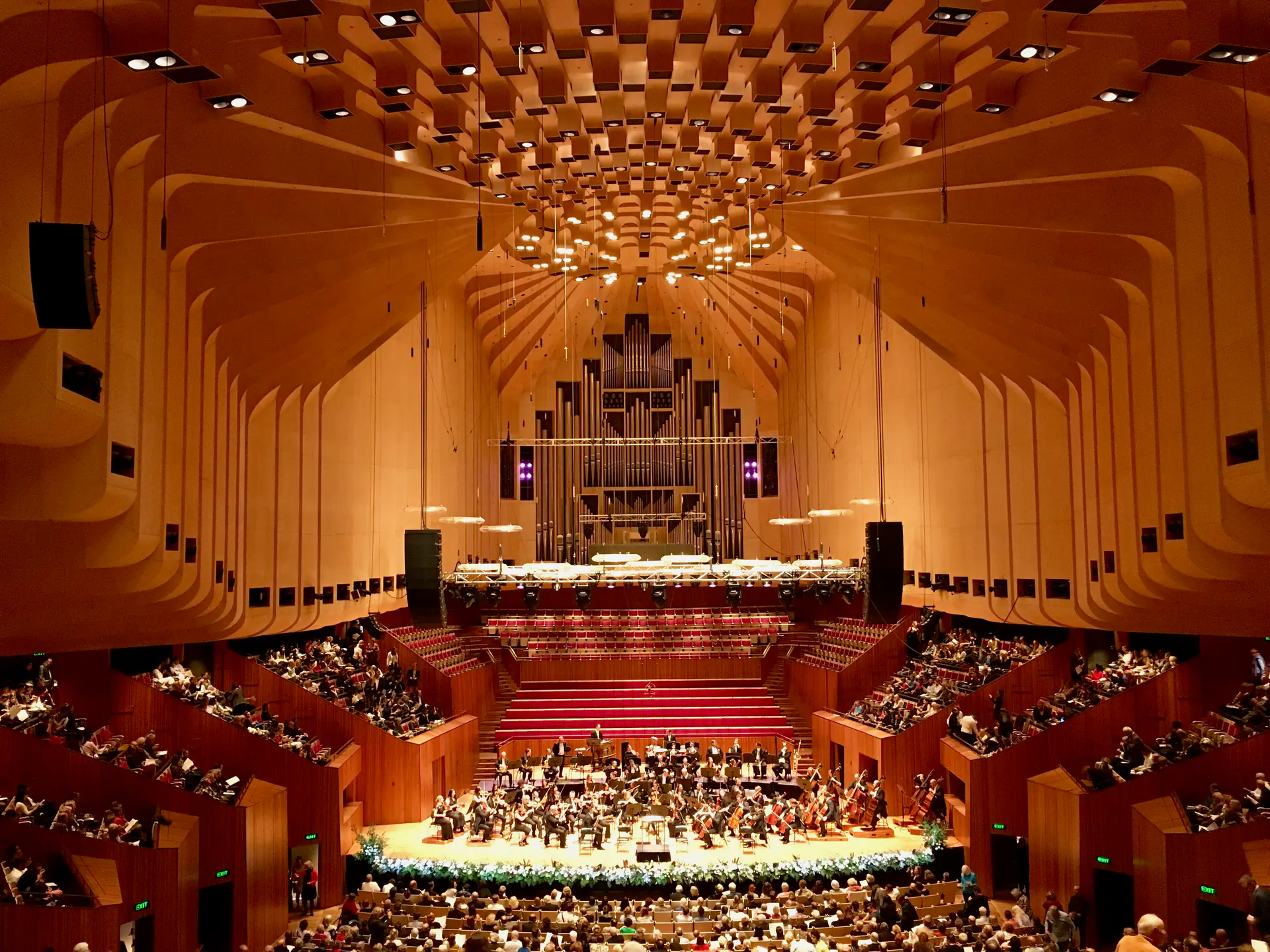 Interior de la Sala de Conciertos de la Ópera de Sídney durante actuación en vivo mostrando audiencia, escenario y reflectores acústicos