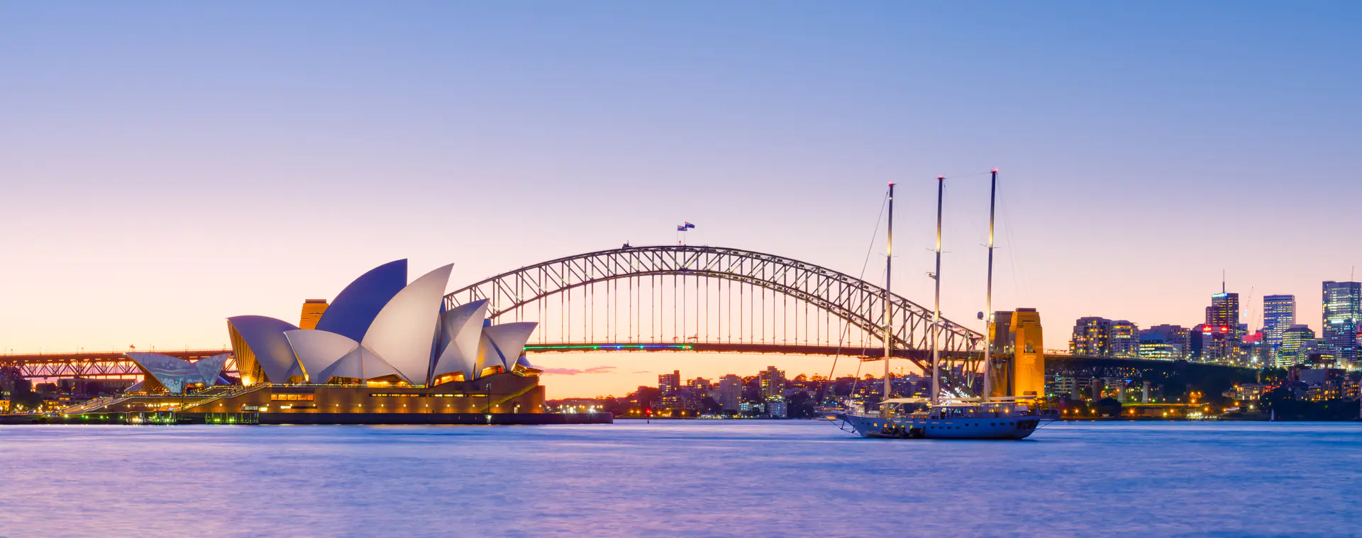 Ópera de Sídney y Harbour Bridge al anochecer con colorido cielo de atardecer reflejado en las aguas del puerto