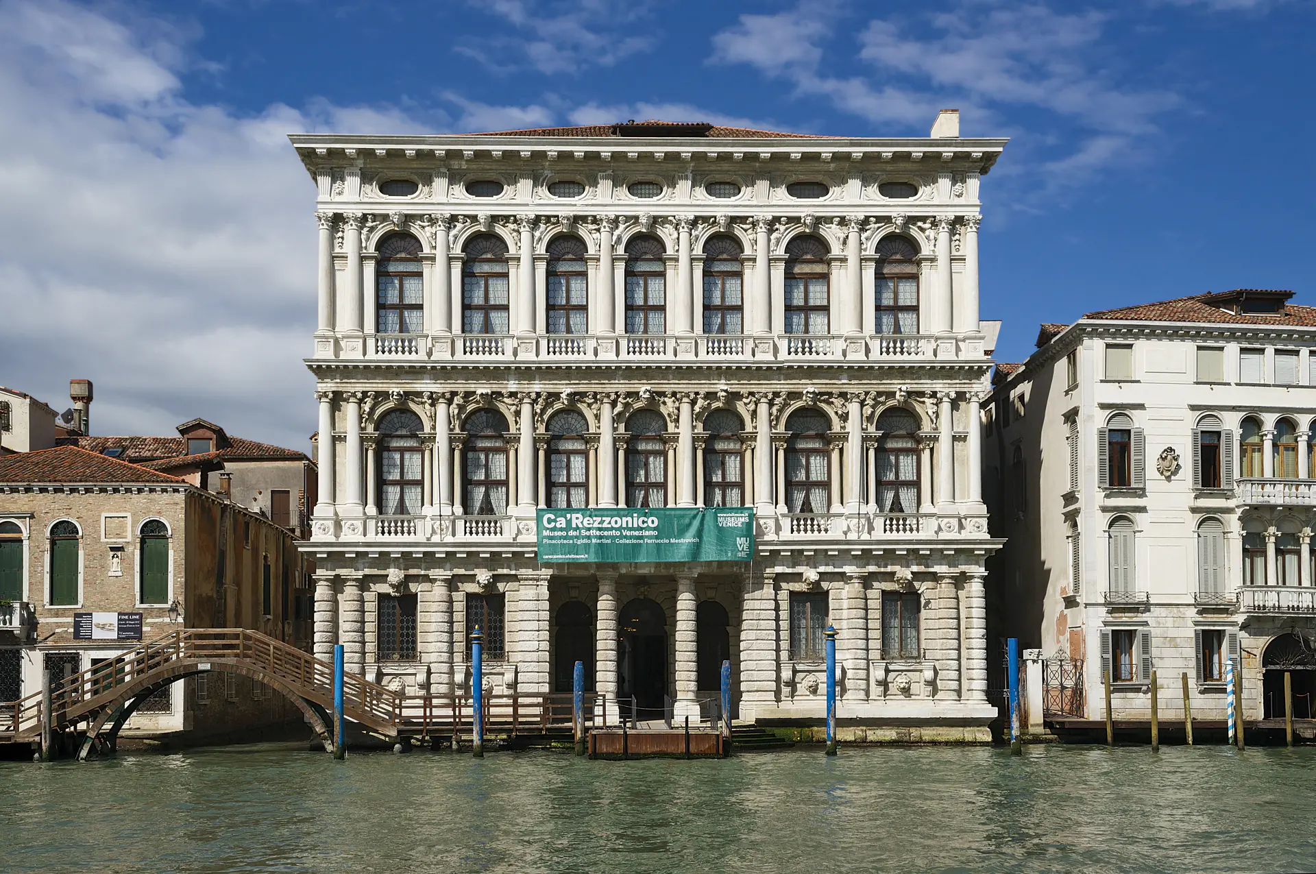 The magnificent white marble facade of Ca' Rezzonico Baroque palace rising from the Grand Canal, showcasing ornate Venetian *palazzo* architecture with multiple levels of arched windows