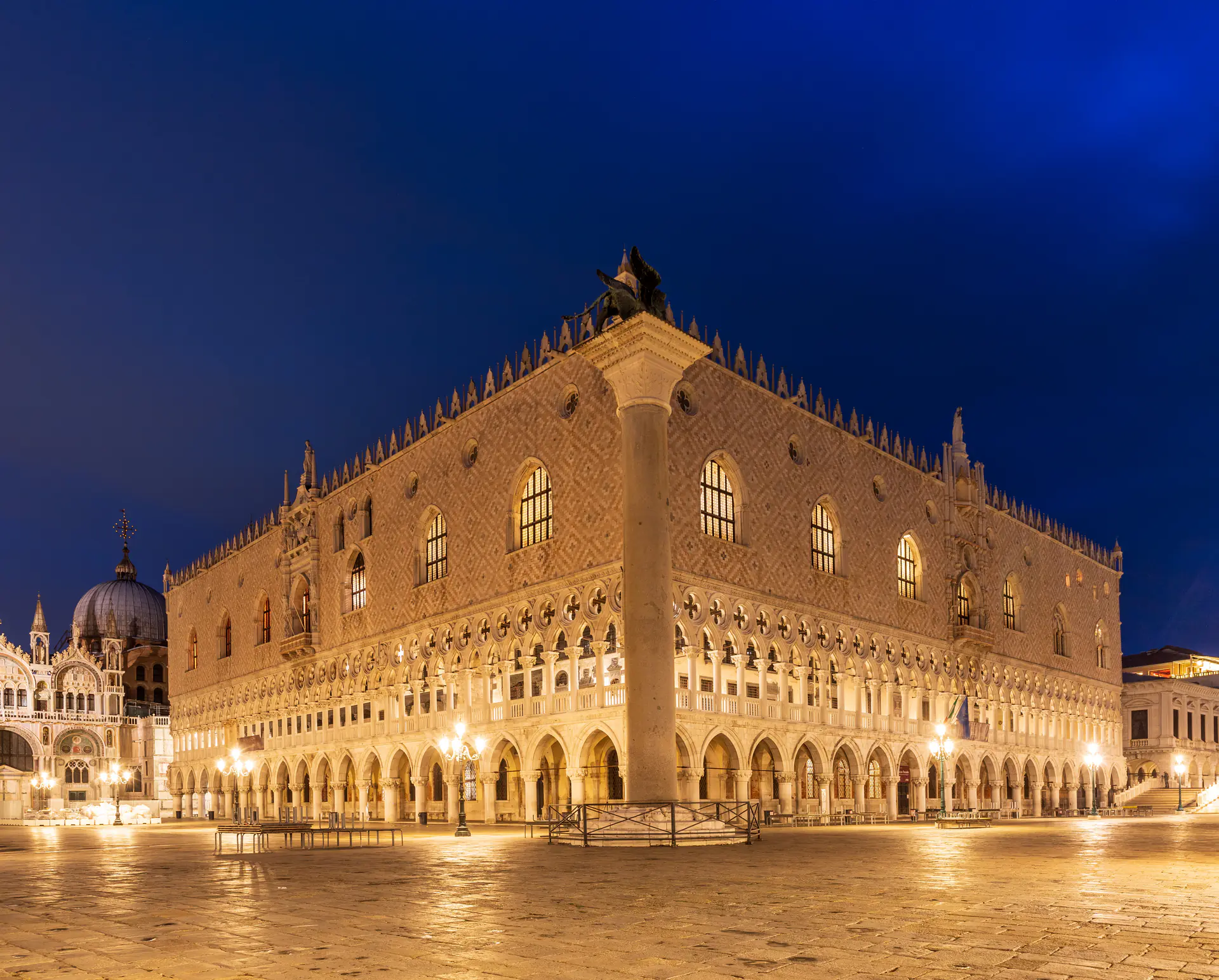 The illuminated Doge's Palace at night with St. Mark's Campanile in the background, captured in dramatic evening light over the Venetian lagoon